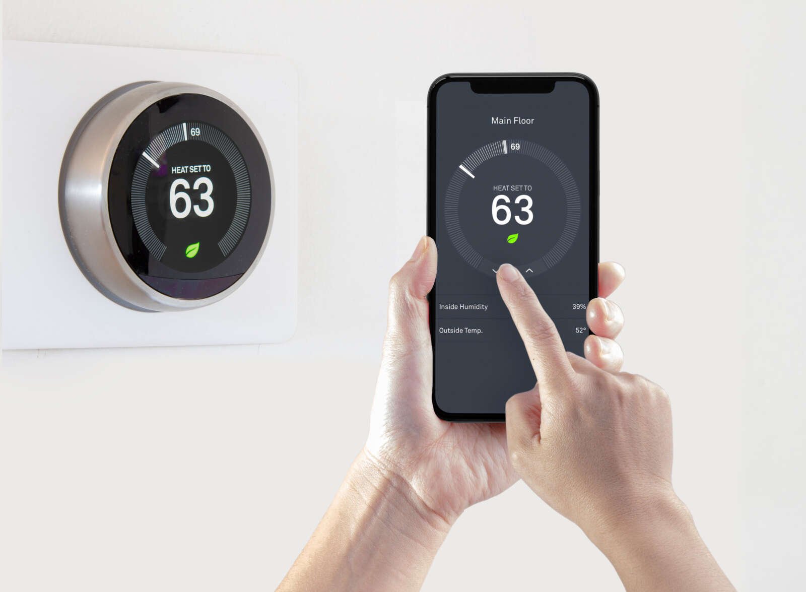 A person is using their smartphone to set a thermostat's temperature